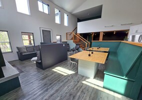 A modern interior with a wooden floor, a black sofa, a wooden dining table, and a green accent wall.