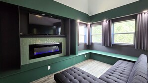A modern room with a large flat-screen TV mounted on the wall, a built-in fireplace, a cushioned bench, and a window with curtains. - Copper Rose Retreat B&B (Invermere)