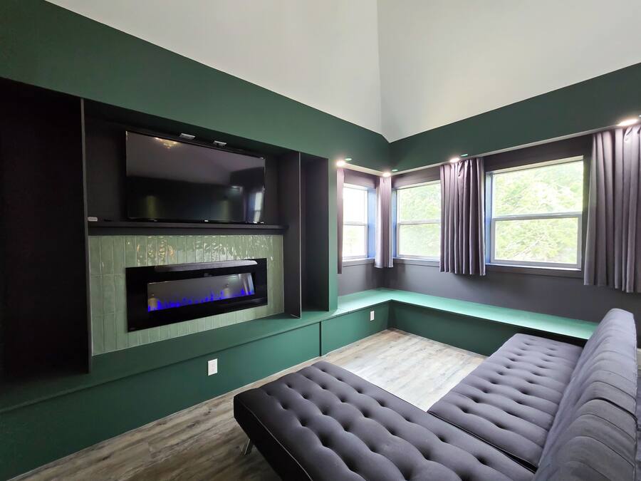 Una habitación moderna con un televisor de pantalla plana grande montado en la pared, una chimenea empotrada, un banco acolchado y una ventana con cortinas.