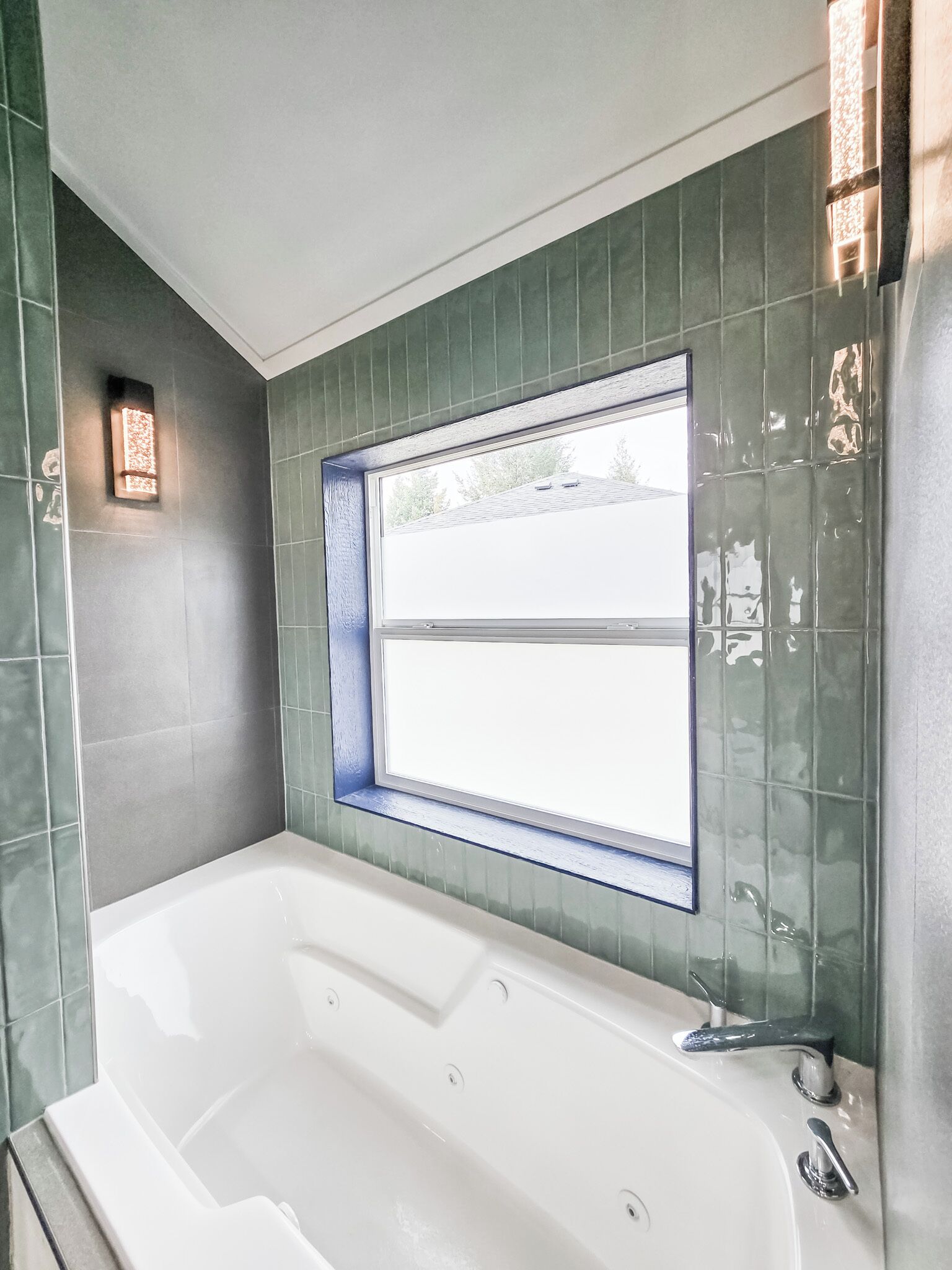 A modern bathroom with a large bathtub, a window, and green tiled walls.