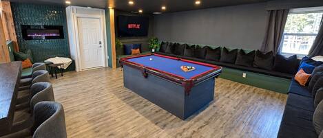 A pool table in a room with a bar, seating area, and a wall-mounted television.