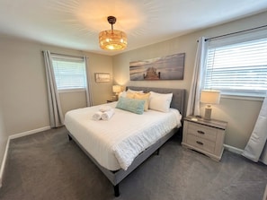 A bedroom with a bed, bedside tables, a lamp, a painting, and a window with curtains.