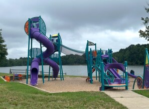 A playground with a purple slide and climbing structures, located near a lake.