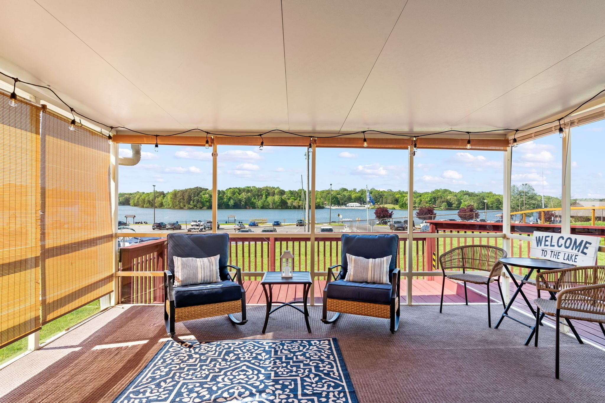 A covered outdoor seating area with wicker chairs and a welcome sign, overlooking a lake with boats.