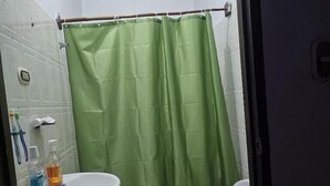 A bathroom with a green shower curtain, a white sink with a soap dispenser, and a toilet with a grey seat. - Hostal Casa Maricel (Granada)