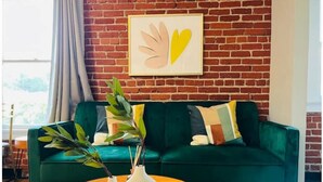 A green sofa with a heart-shaped painting above it, a round wooden table with two white vases, and a plant with green leaves. - Hollywood sign view/ 5 mins from universal studio (West Hollywood)
