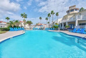 Piscina con sillones reclinables azules y palmeras al fondo.