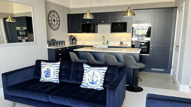 Een moderne woonkamer met een donkerblauwe bank, een salontafel en een grote spiegel.