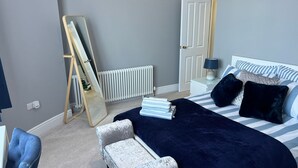 Een slaapkamer met een bed, nachtkastje, lamp en spiegel.