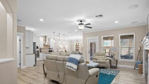 A spacious living room with a beige sectional sofa, a ceiling fan, and a kitchen in the background. - Laguna Getaway Boater & Pet Friendly Canal Home (Corpus Christi)