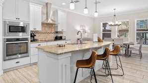 A modern kitchen with white cabinets, stainless steel appliances, a granite countertop, and bar stools. - Laguna Getaway Boater & Pet Friendly Canal Home (Corpus Christi)