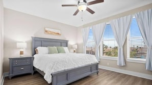 A bedroom with a bed, nightstands, a ceiling fan, and large windows with curtains. - Laguna Getaway Boater & Pet Friendly Canal Home (Corpus Christi)