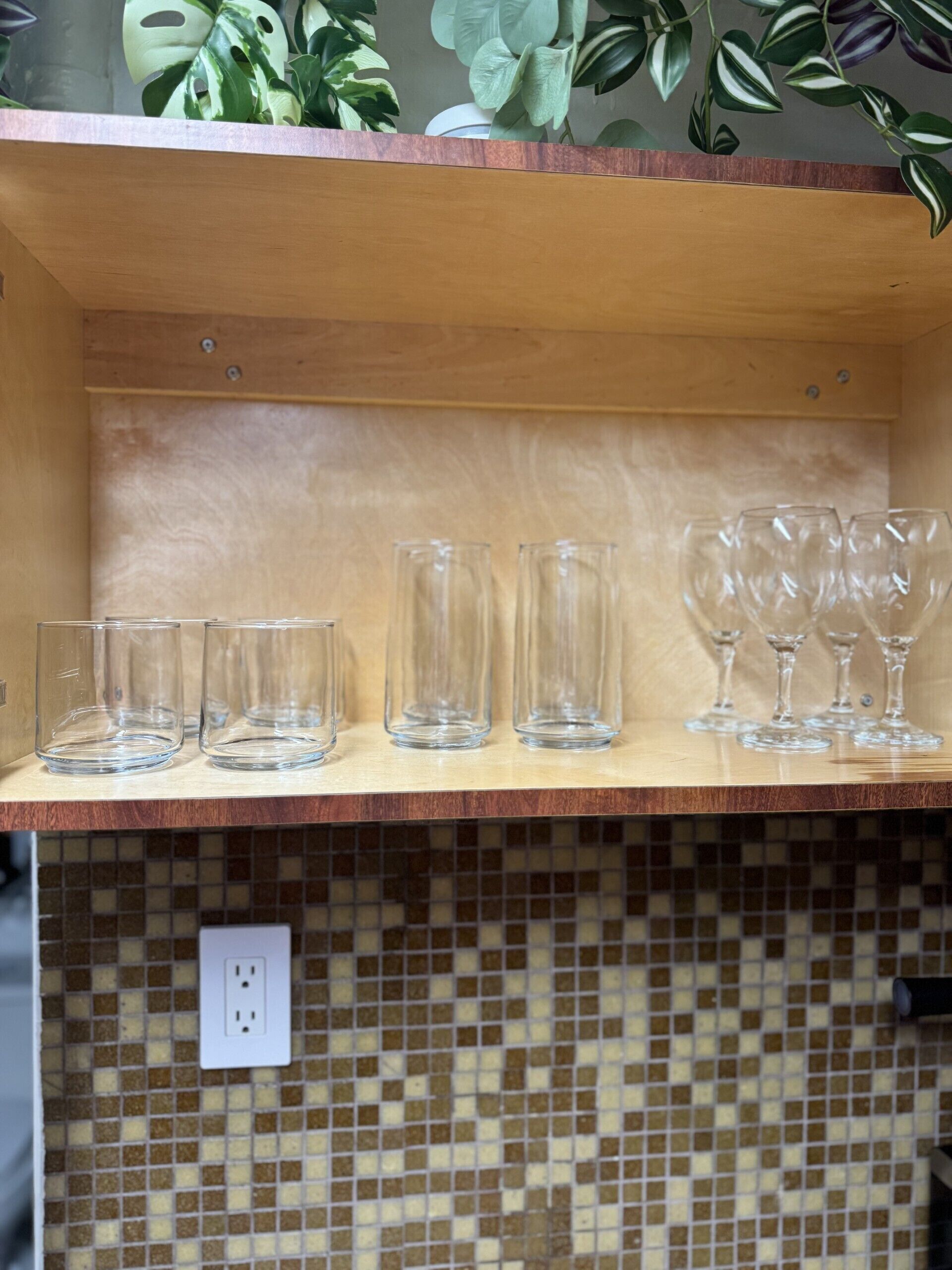 A shelf with various glassware, including tumblers and wine glasses, in a room with a tiled backsplash.