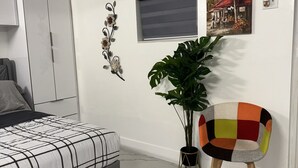 A bedroom with a bed, a chair, a potted plant, and a wall with a window and artwork. - Sol studio in the middle of Miami (Miami)