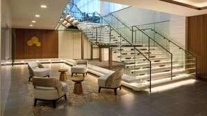 Un vestíbulo moderno con una escalera de cristal, zona de estar y vistas a la ciudad.