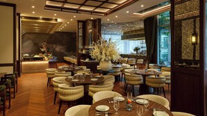 Un restaurante espacioso con varias mesas, sillas cómodas y un jarrón grande con flores.