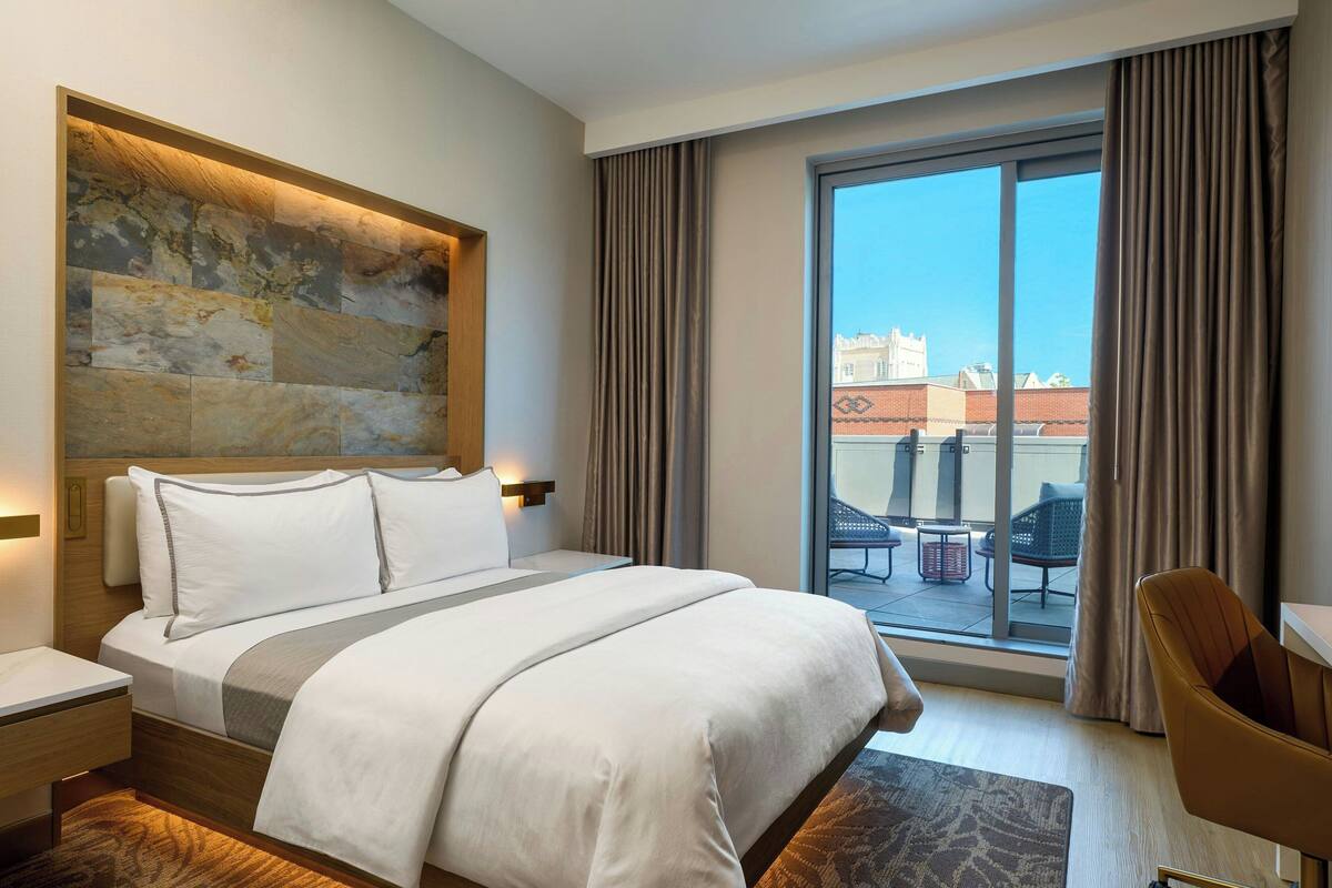 A hotel room with a large bed, a view of the city through a sliding glass door, and a modern headboard.