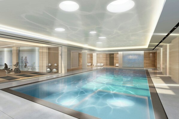 A modern indoor swimming pool with clear water, surrounded by glass walls and wooden paneling.