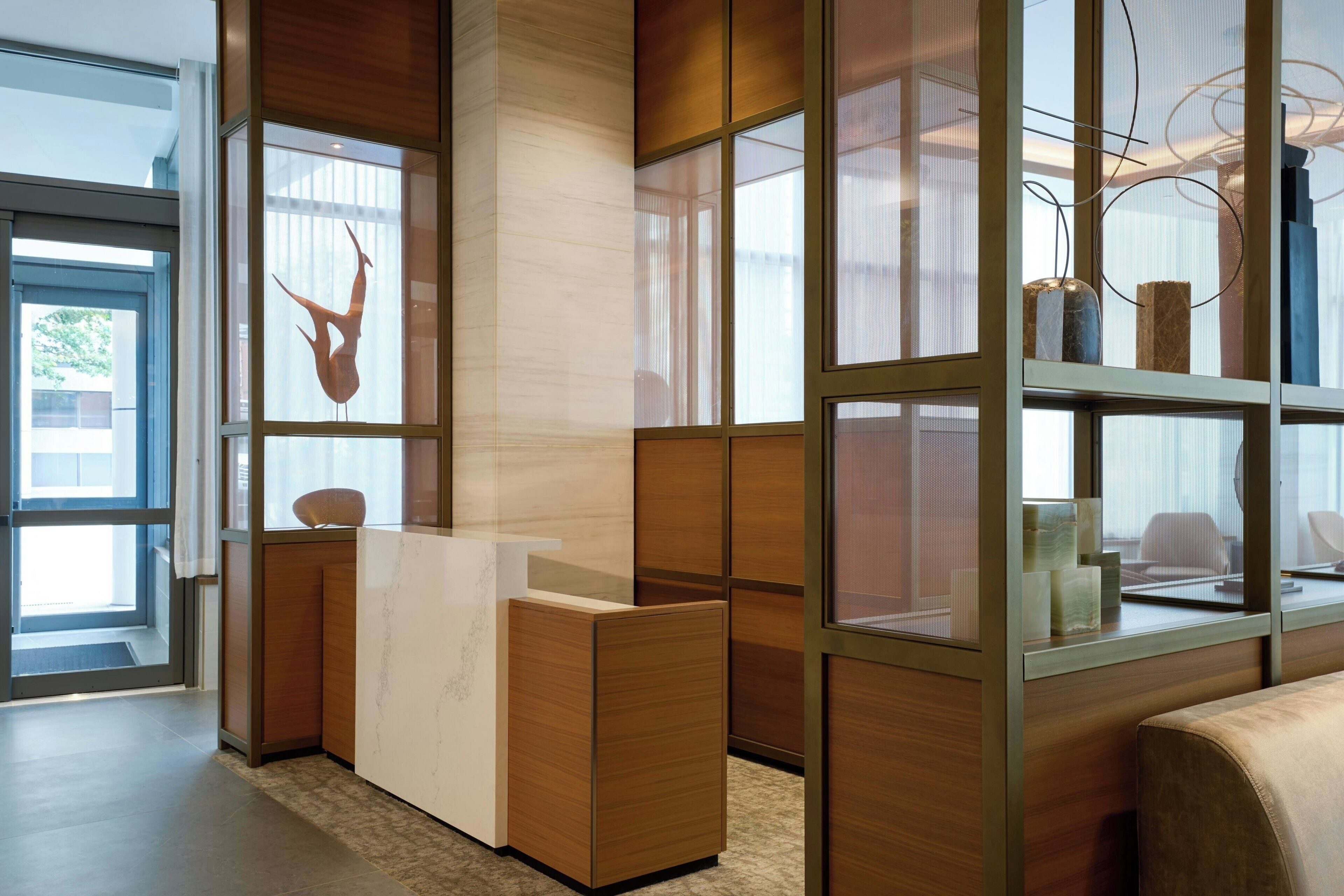 A modern reception area with a wooden reception desk, a glass partition, and a view of the outdoors.