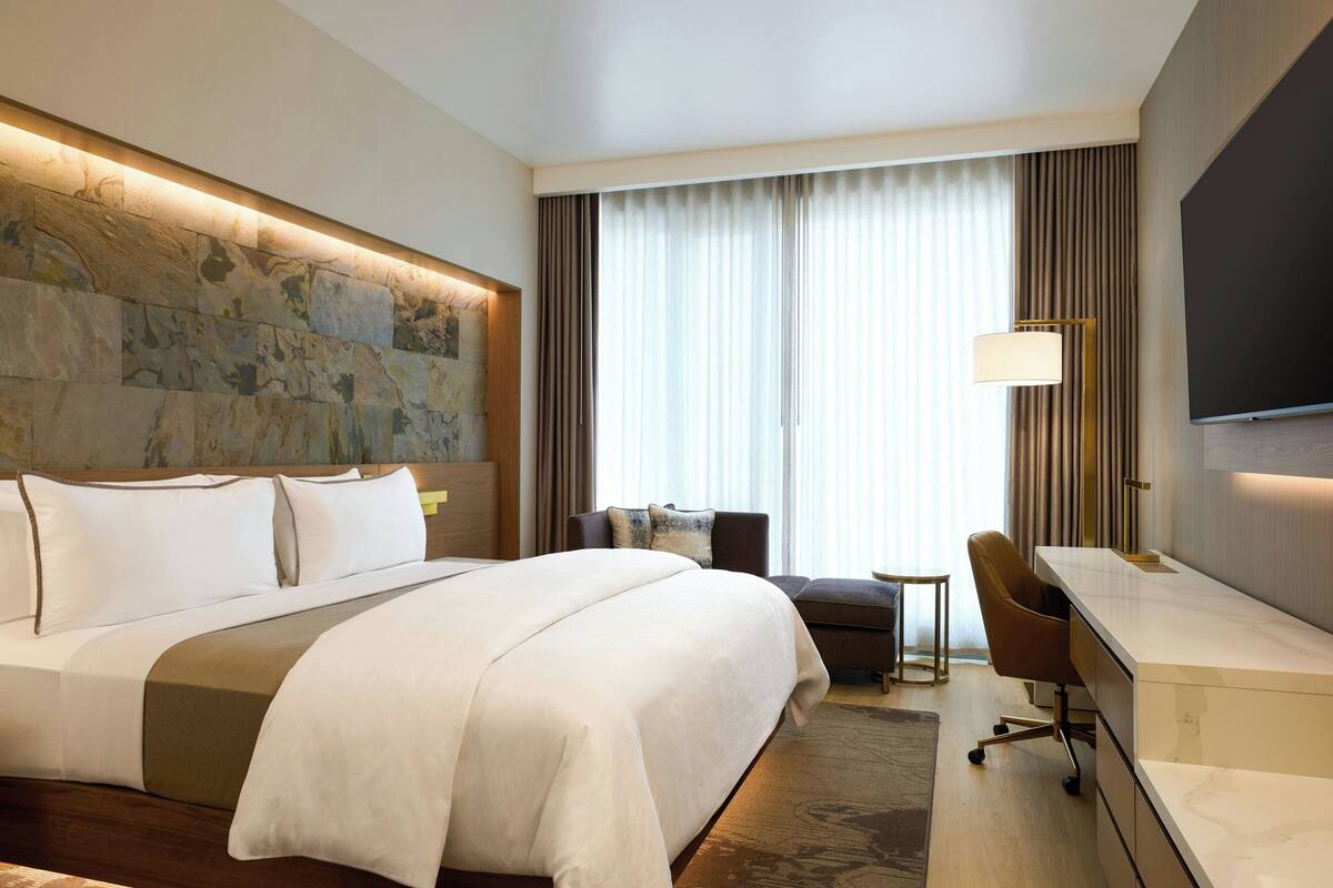 A hotel room with a large bed, a desk with a chair, a television, and a window with curtains.