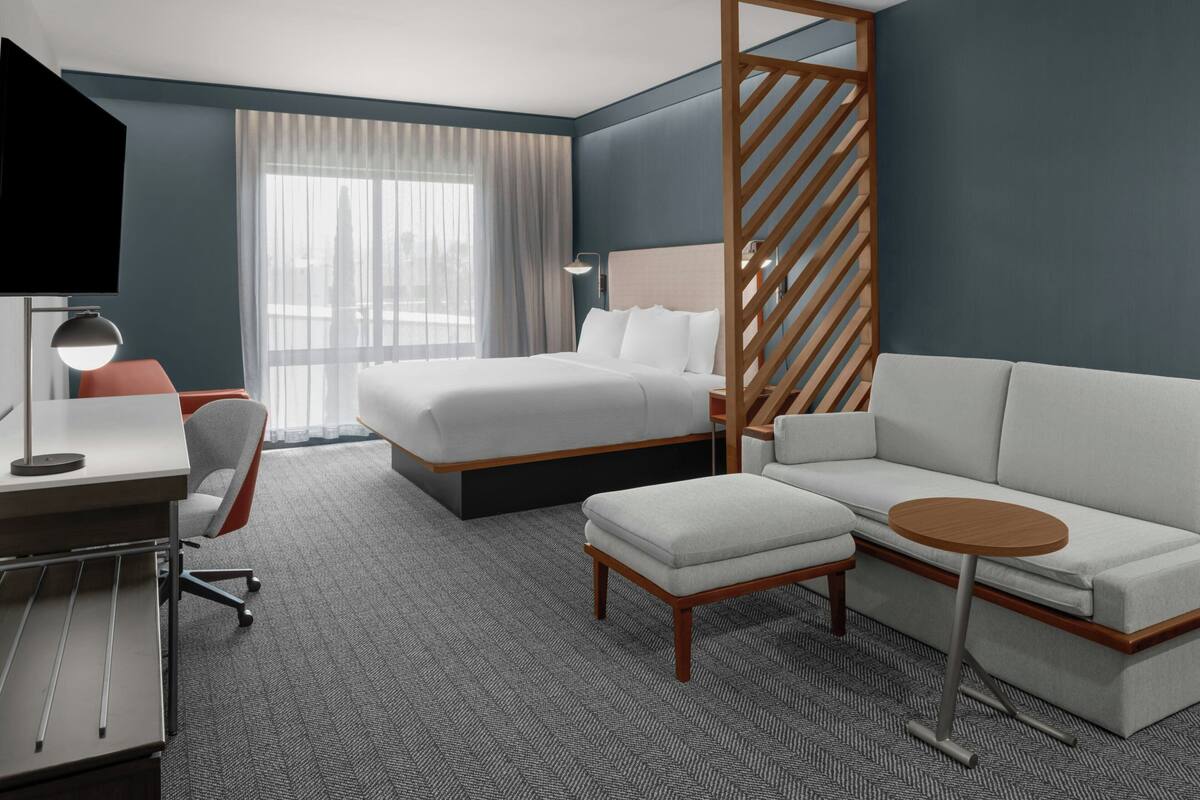 A modern hotel room with a bed, a sofa, a desk, and a TV.