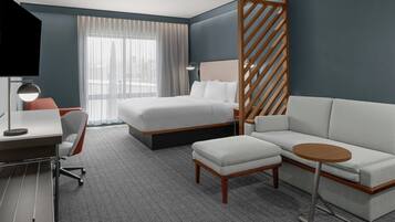 A modern hotel room with a bed, a sofa, a desk, and a TV.