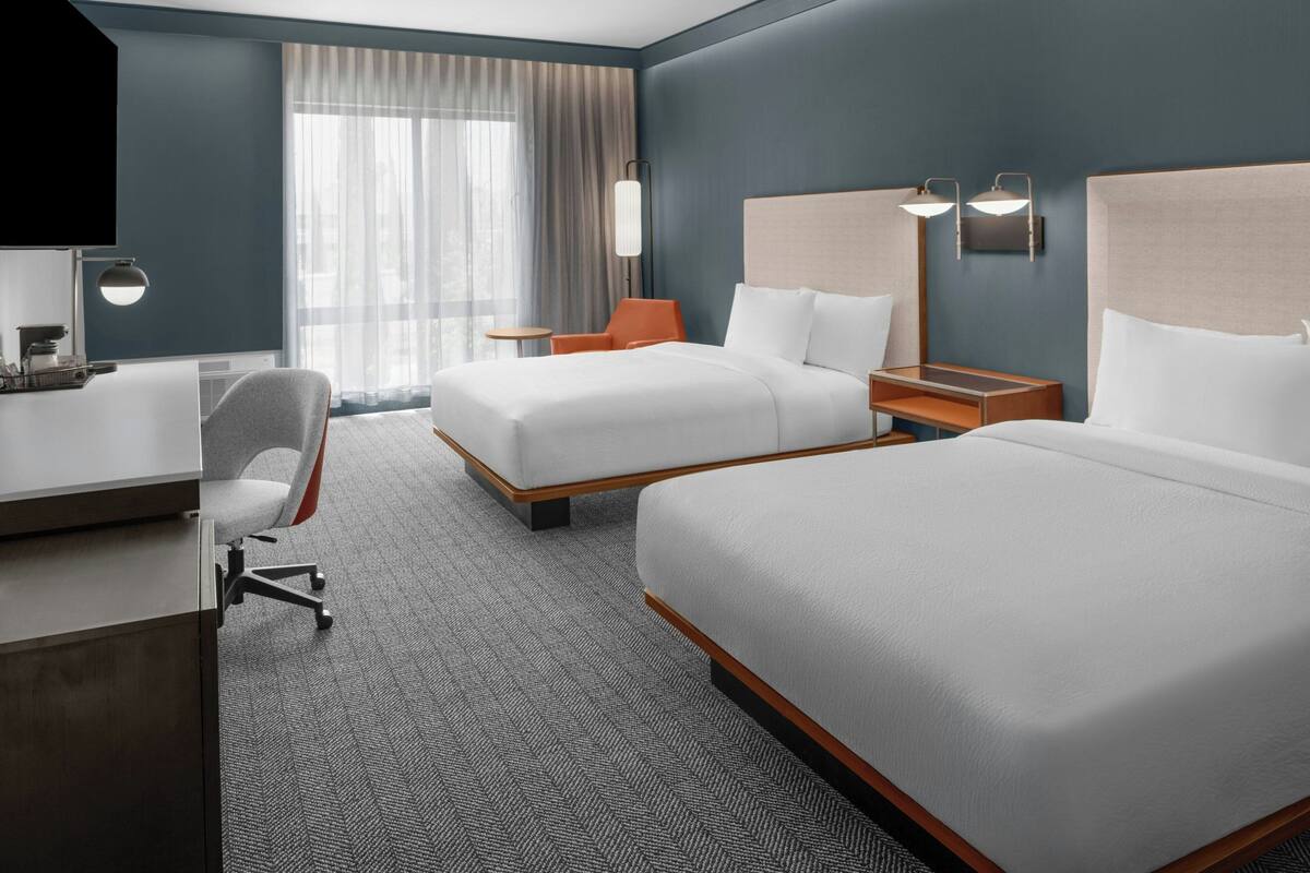 A hotel room with two beds, a desk, a chair, and a TV.