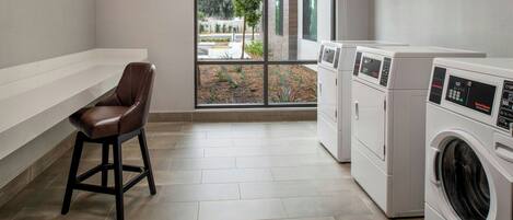A laundry room with a chair, washing machines, and a view through a large window.