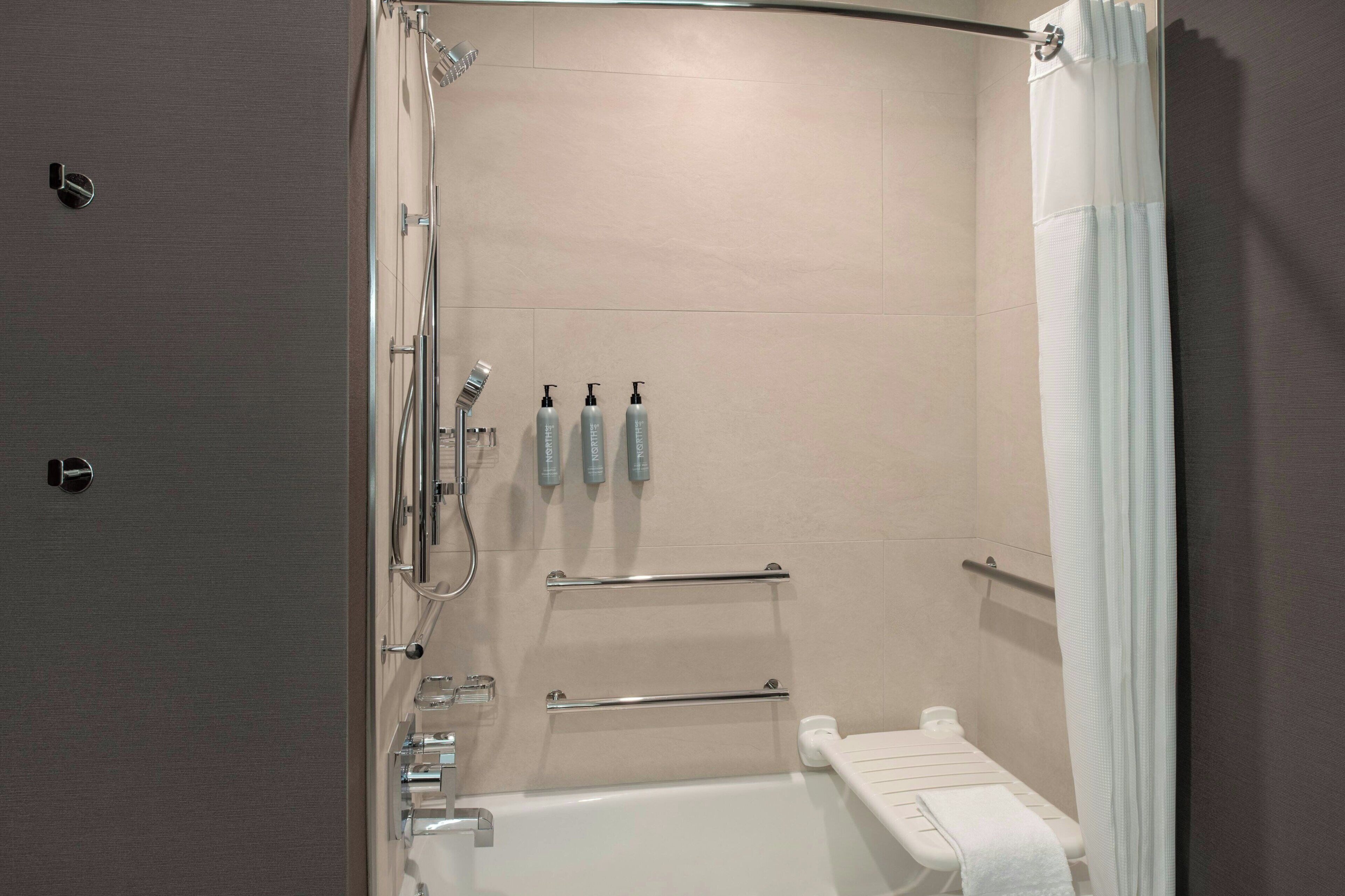 A modern bathroom with a shower, toilet, and handrails.