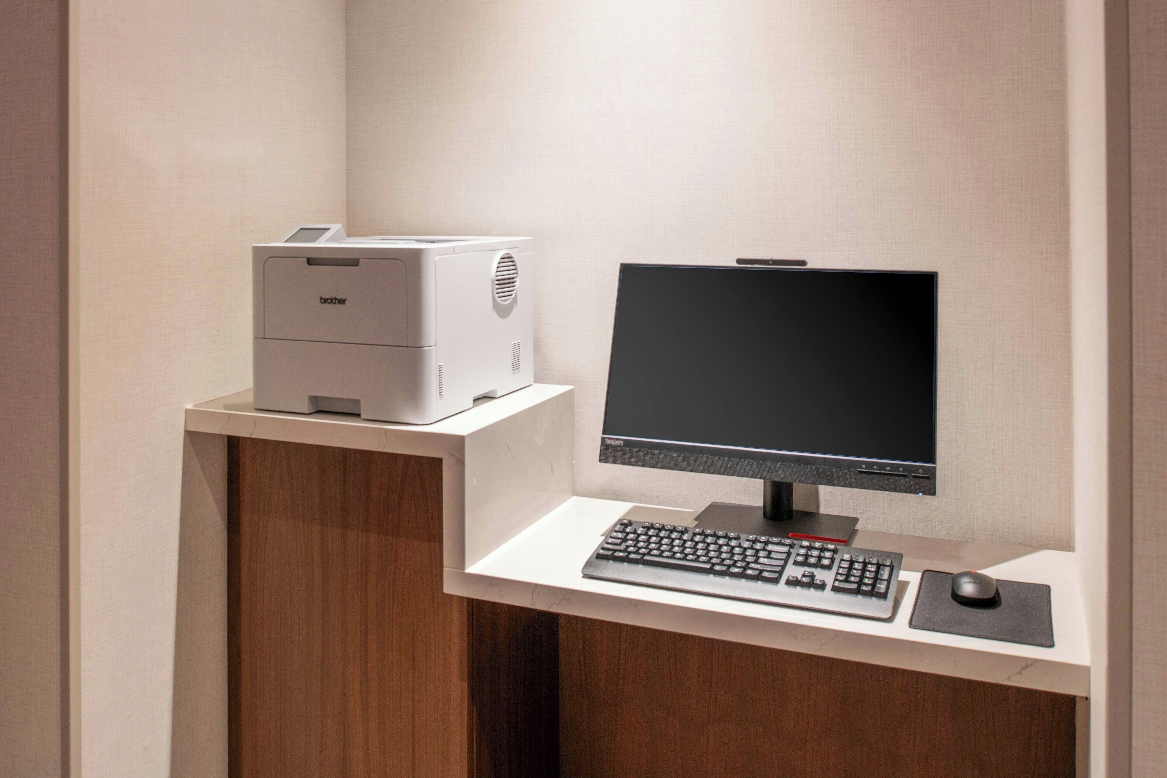 Un bureau moderne équipé d’une imprimante Brother, d’un écran plat, d’un clavier et d’une souris, le tout posé sur un bureau blanc.