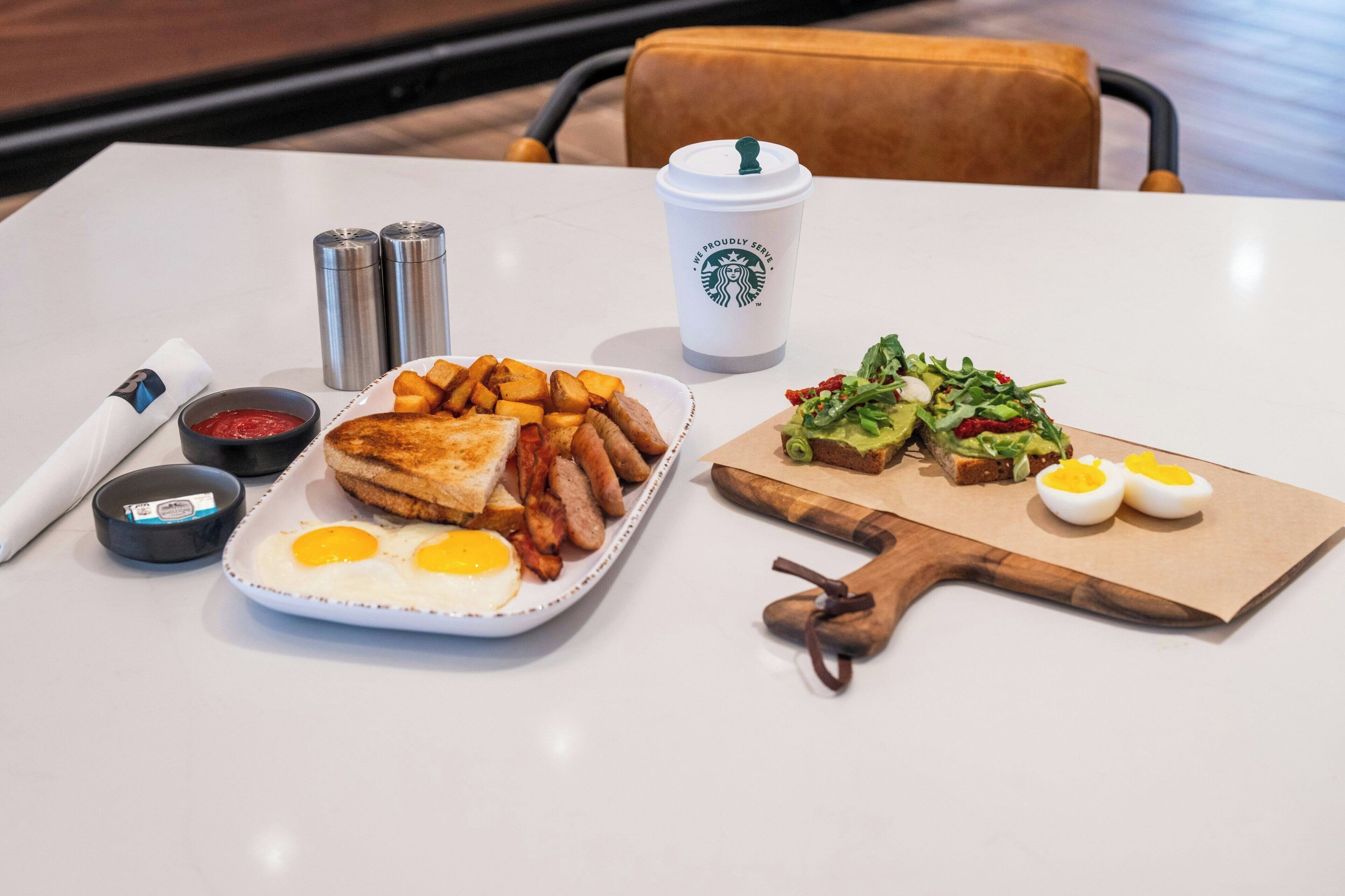 Une table avec des aliments pour le petit-déjeuner, notamment des toasts, des œufs, des saucisses et une salade.