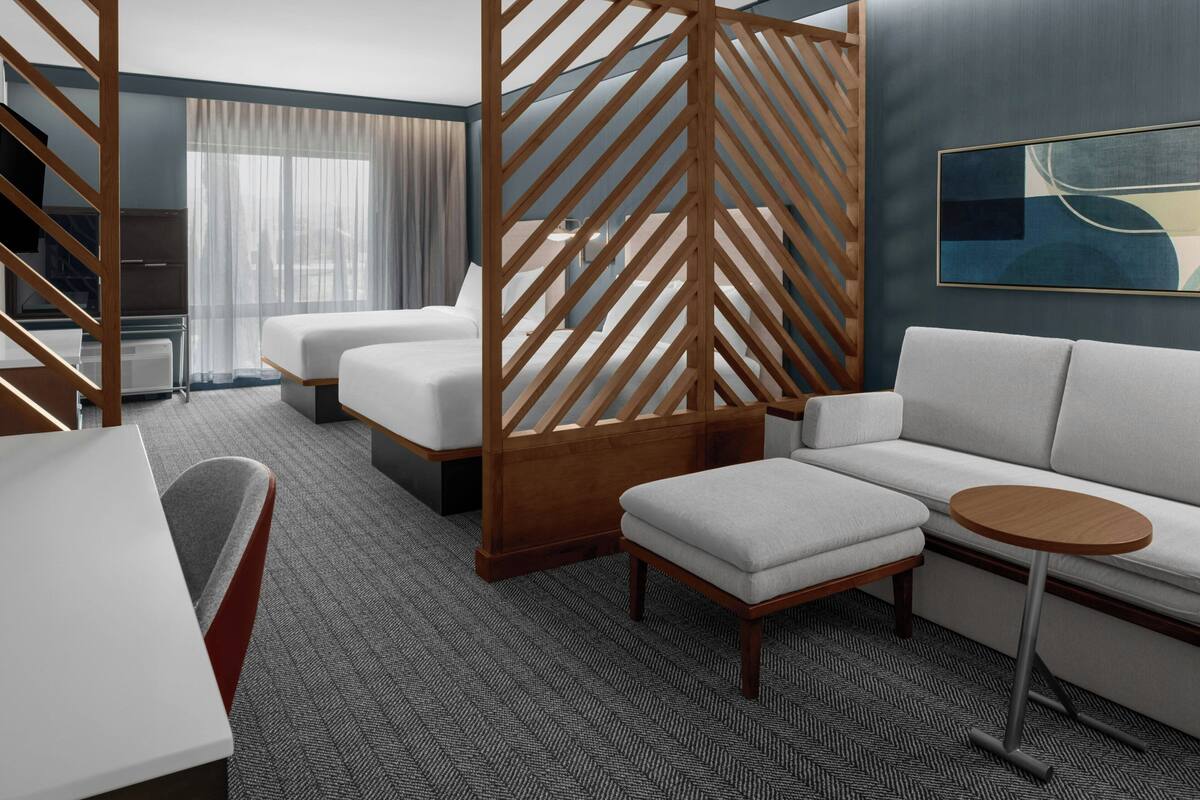 A hotel room with a sofa, two beds, a small table, and a TV.
