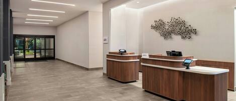 A hotel reception area with a modern design, featuring wooden reception desks and a wall-mounted decorative piece.