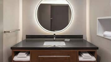 A modern bathroom with a round mirror, dark countertop, and wooden cabinet with towels.