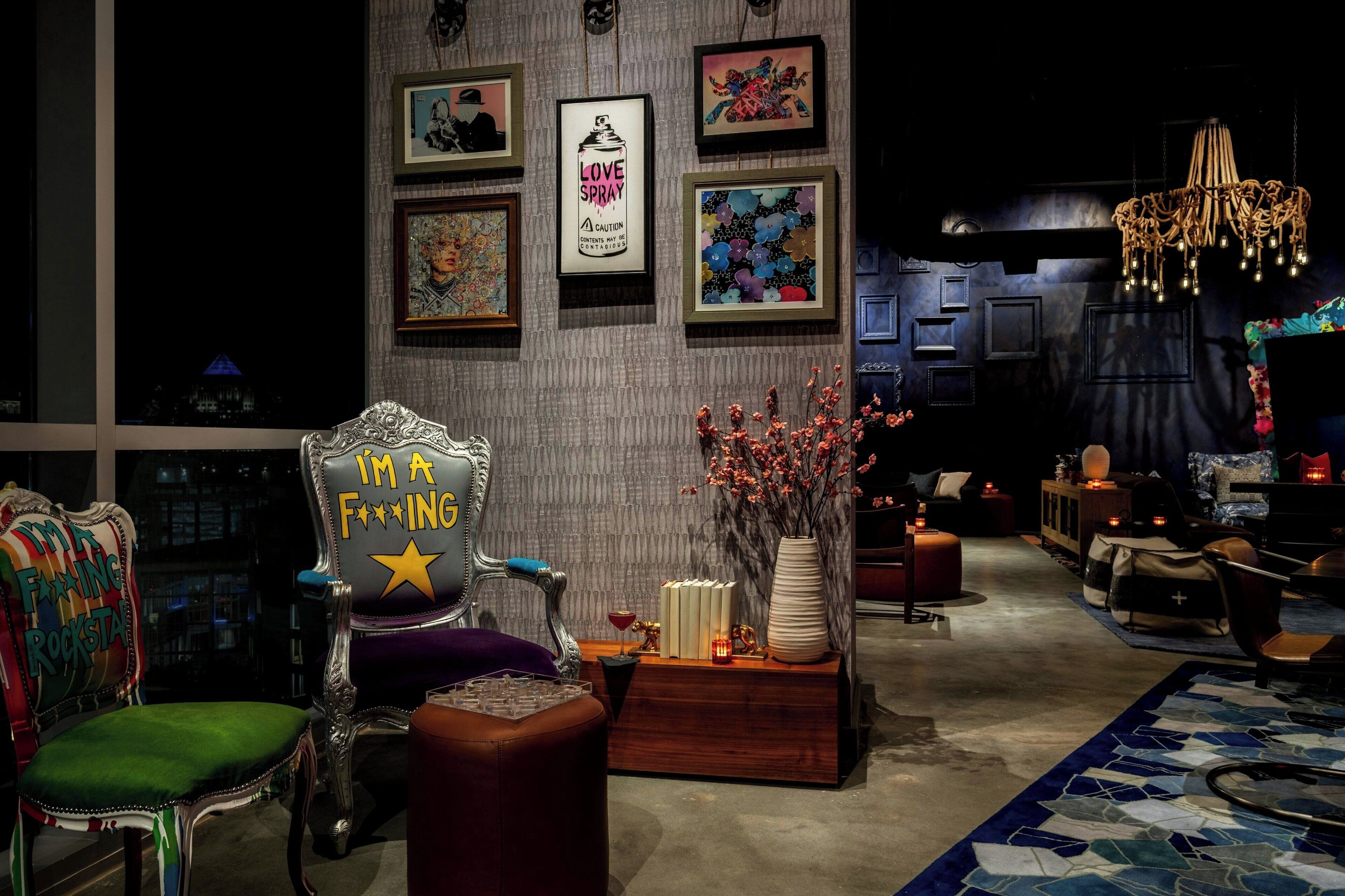 A modern living room with a large ornate chair, a chandelier, and various framed artworks on the wall.