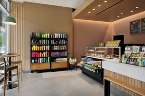 A modern coffee shop interior with a counter, seating area, and a variety of products on shelves. - Moxy Charlotte Downtown (Charlotte)