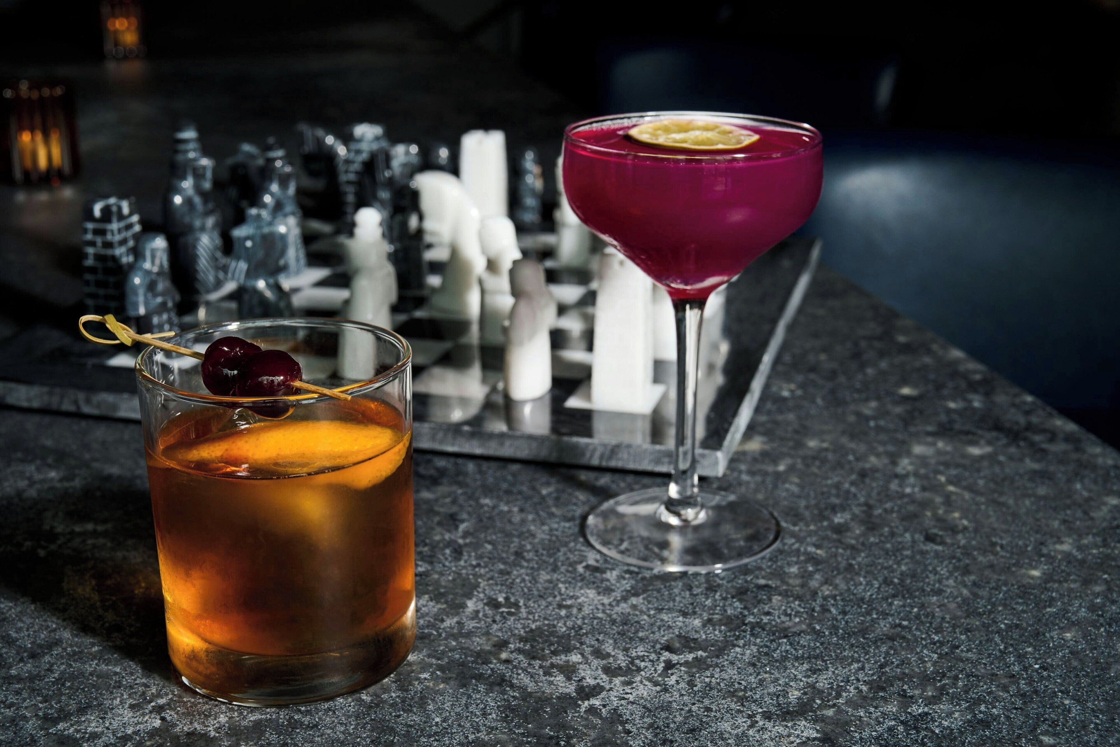 Two drinks on a bar counter with salt and pepper shakers and a decorative item in the background.