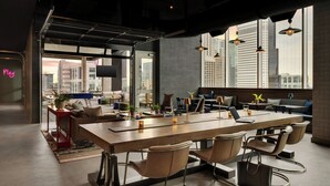 A modern dining area with a long table, multiple chairs, and a city view through large windows.