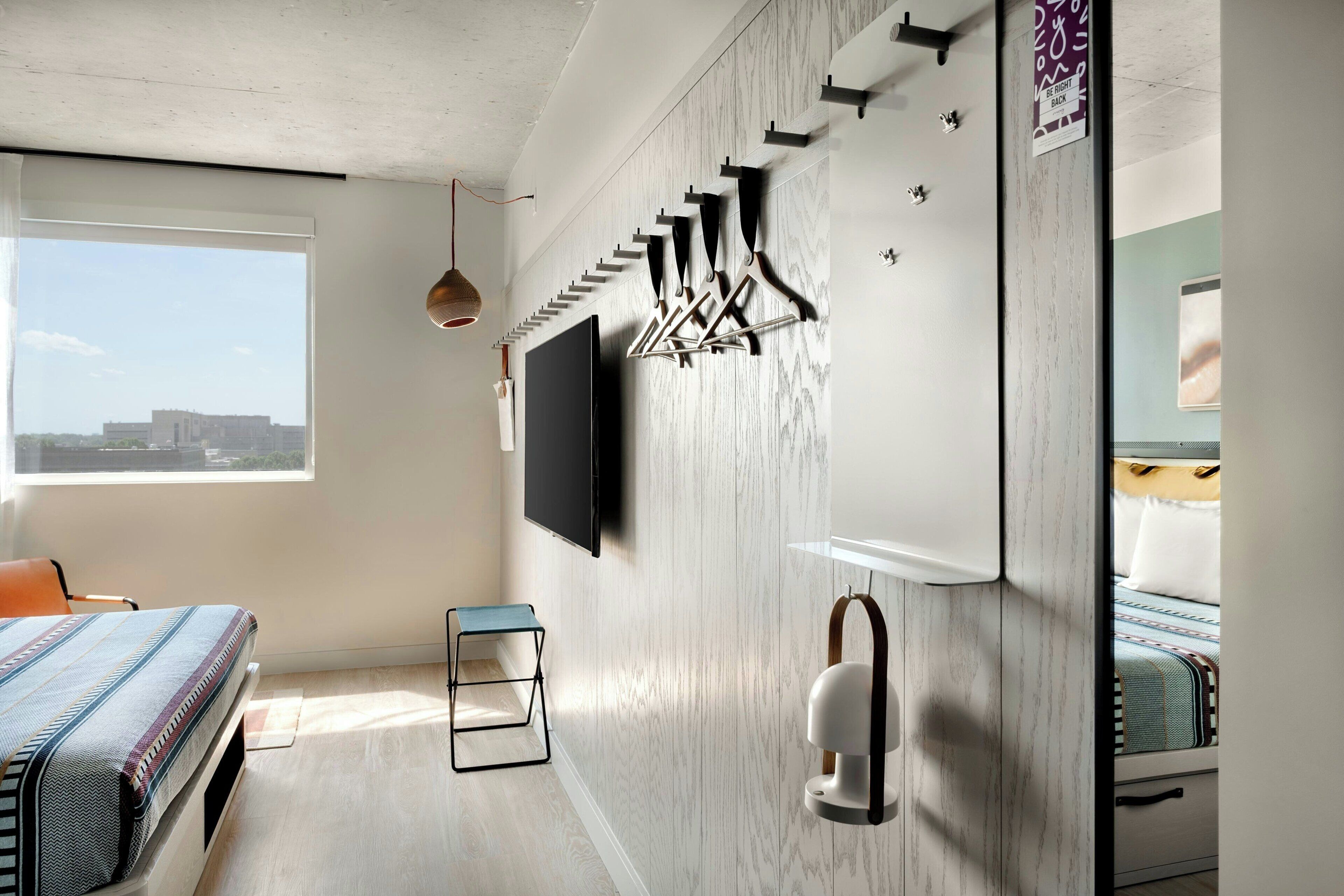 Una habitación de hotel moderna con una cama grande, un televisor montado en la pared, un armario de madera y una ventana con vistas a la ciudad.