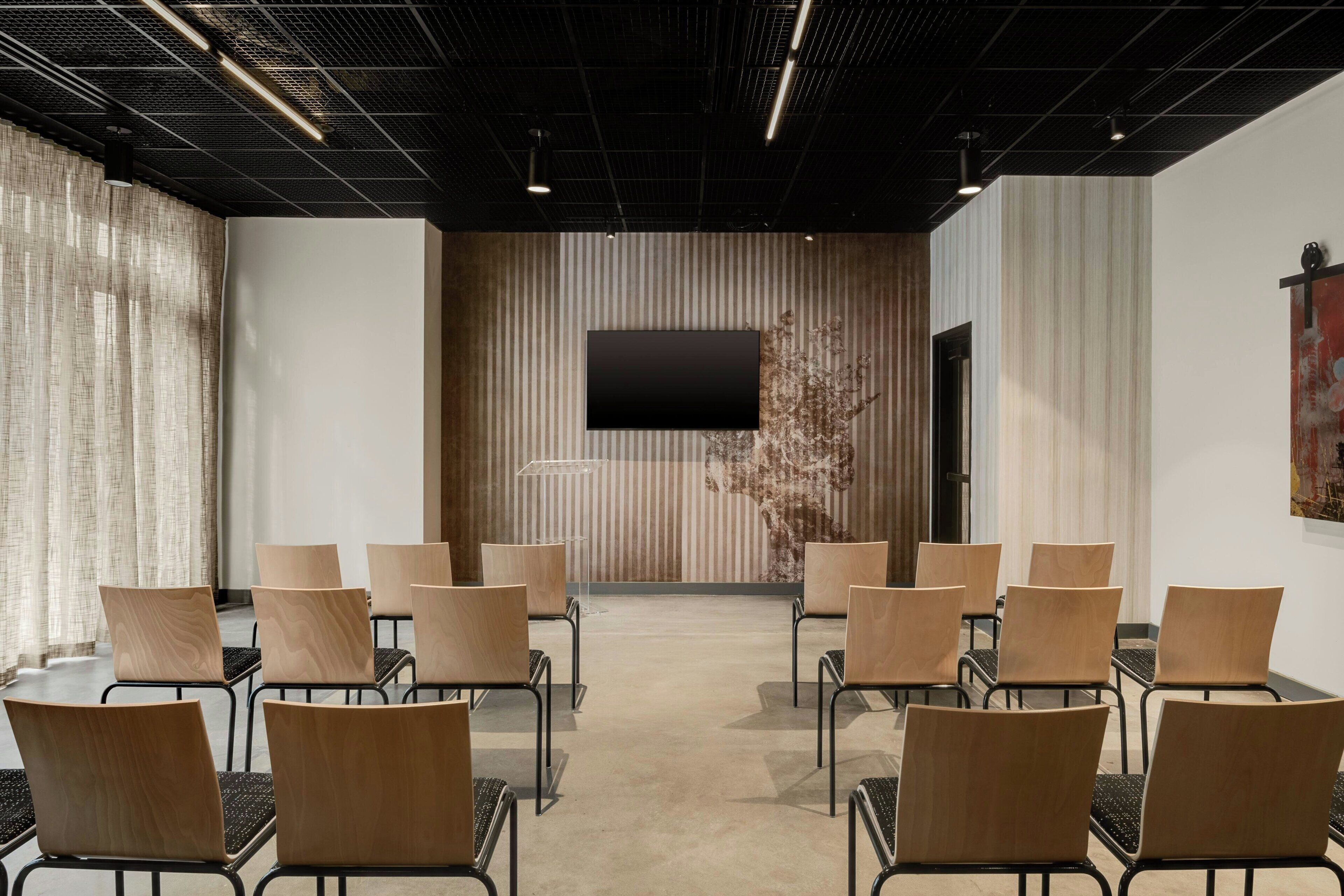 A conference room with a modern design, featuring a large flat-screen TV mounted on a wooden panel wall, surrounded by rows of wooden chairs with black frames.