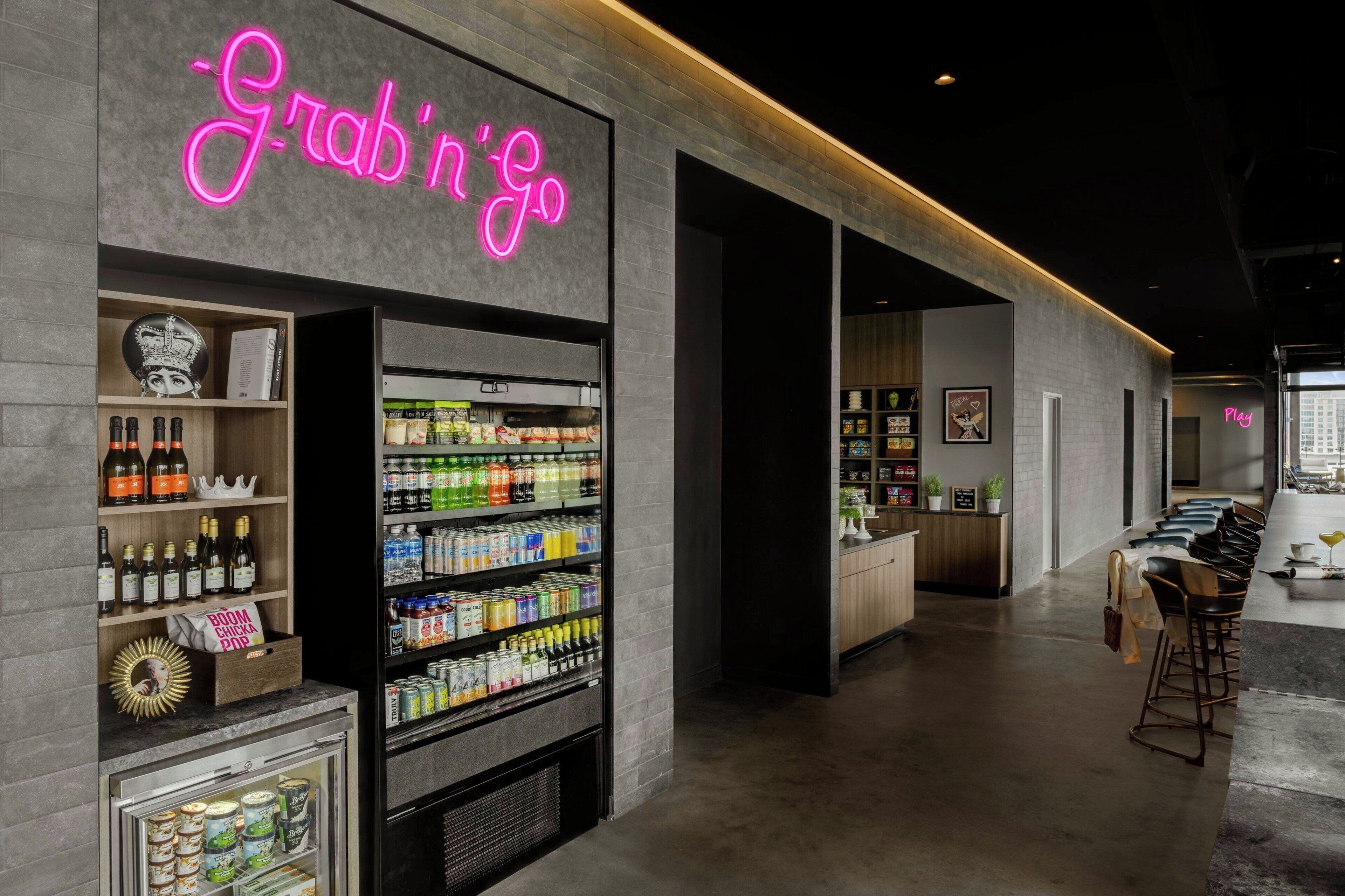 A modern bar area with a neon sign reading "Grab 'n' Go," shelves stocked with various beverages, and a bar counter with stools.