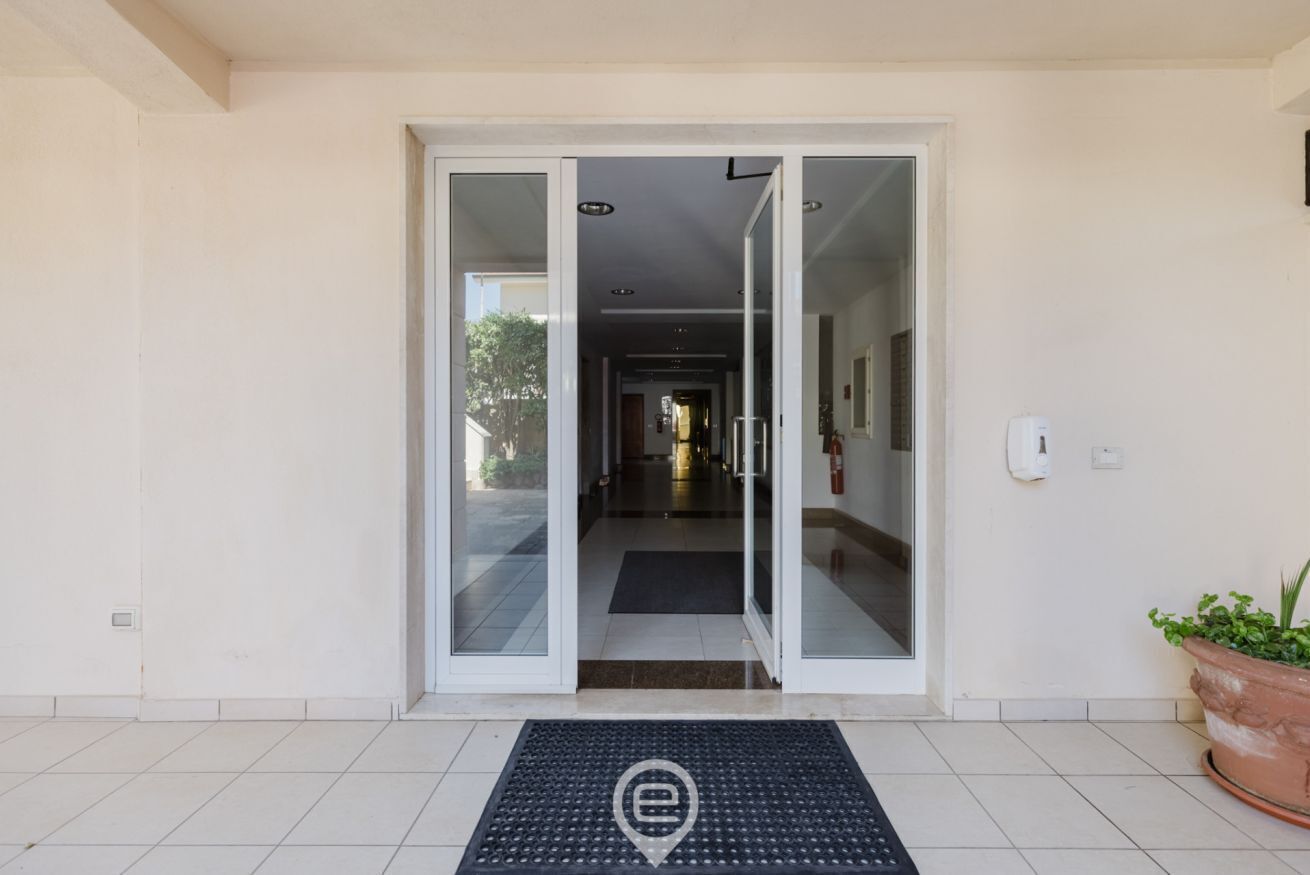 L’entrée d’un hôtel, avec une porte en verre, un paillasson et une plante en pot.