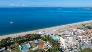 An aerial view of a coastal area with a beach, a sailboat, and a building complex with multiple structures. - Pine & Sea Hideaway - Torre Grande (Torre Grande)