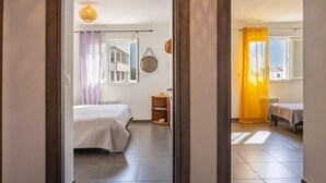 A bedroom with a bed, a small wooden nightstand, a window with a view, and a curtain. - Casa Verde (San-Nicolao)
