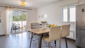 A modern kitchen with a dining table, chairs, a scale, and a refrigerator. - Casa Verde (San-Nicolao)