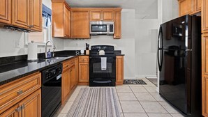 A modern kitchen with wooden cabinets, a stainless steel refrigerator, a stove, and a microwave. - Charming Bungalow with Spacious Yard (Overland Park)