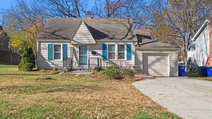A single-story house with a garage, a front porch, and a small front yard. - Charming Bungalow with Spacious Yard (Overland Park)