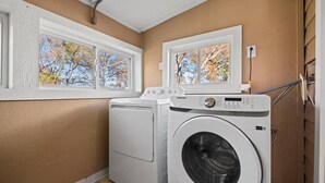 A laundry room with a front-loading washer and dryer, a window with a view of trees, and a white ceiling. - Charming Bungalow with Spacious Yard (Overland Park)
