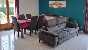 A living room with a sofa, dining table, chairs, and a painting on the wall. - Less than 10 minutes from the ocean! 5-Bedroom Family Villa with Air Conditioning, Wi-Fi, and a Pool (Claira)