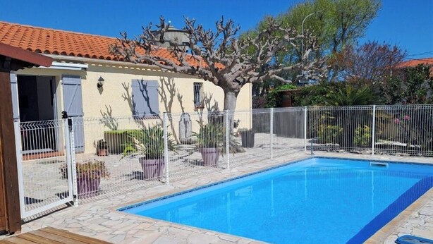 A swimming pool with a wooden deck, surrounded by a fence, and a building with a tiled roof in the background. - Less than 10 minutes from the ocean! 5-Bedroom Family Villa with Air Conditioning, Wi-Fi, and a Pool (Claira)